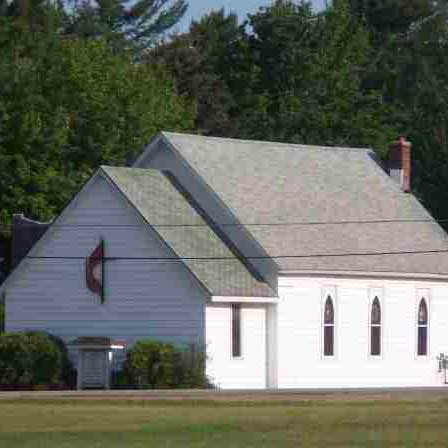 White church building with green roof and trees.