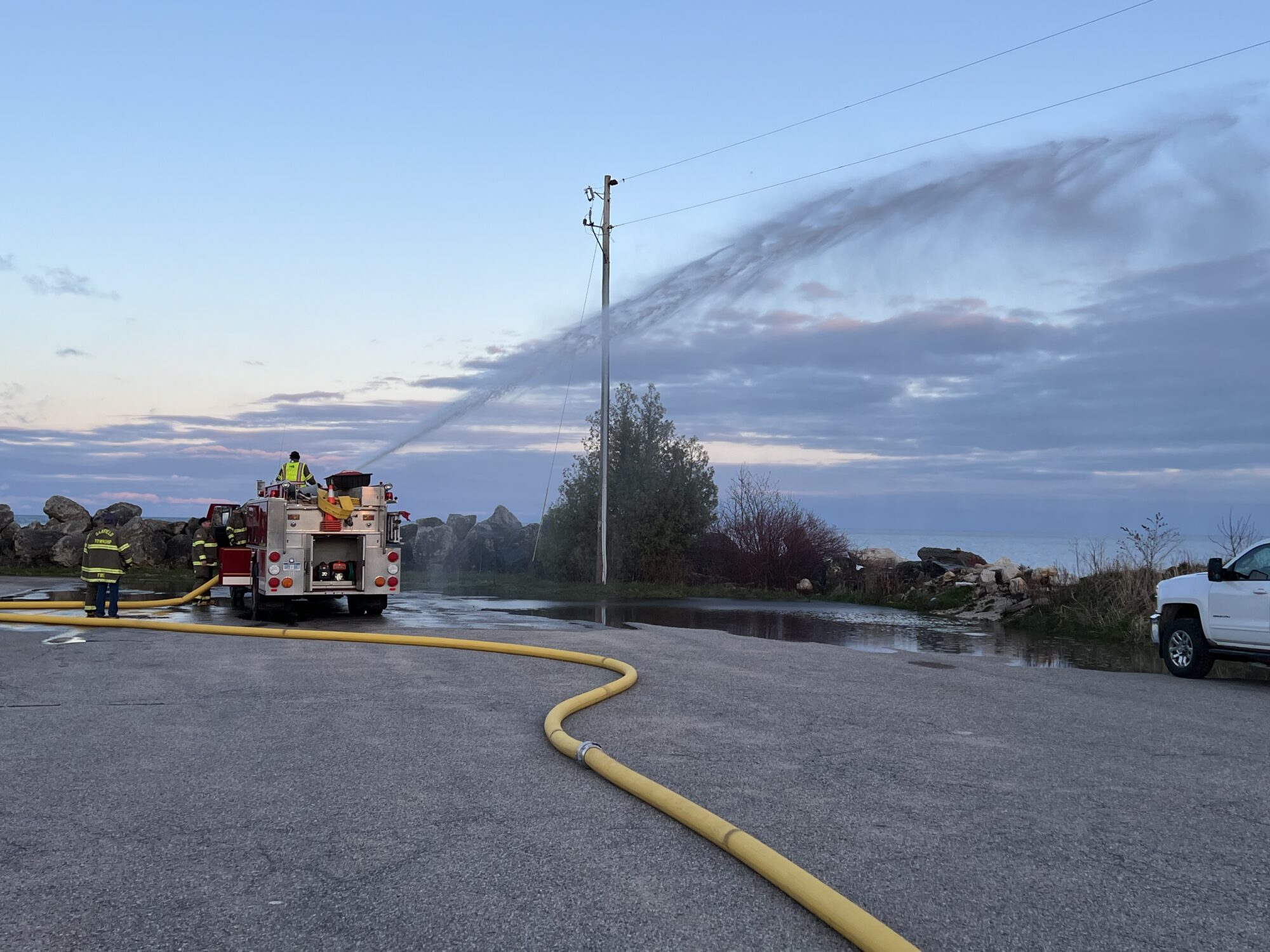 Firefighters using hose to spray water at sunset.