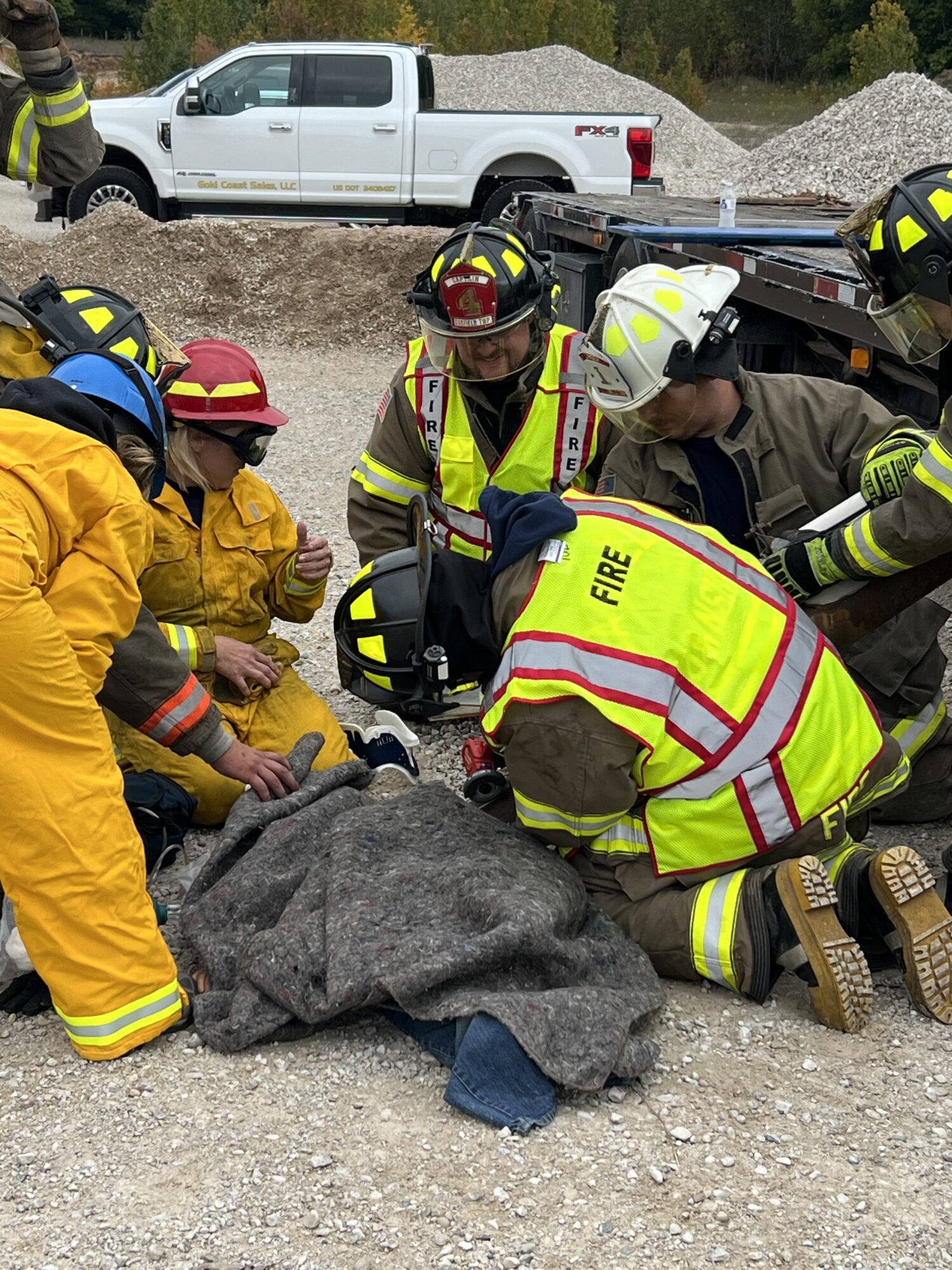 Firefighters assist person on gravel ground.