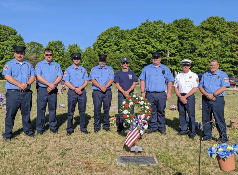 Firefighters honoring memorial with floral tribute and flags.